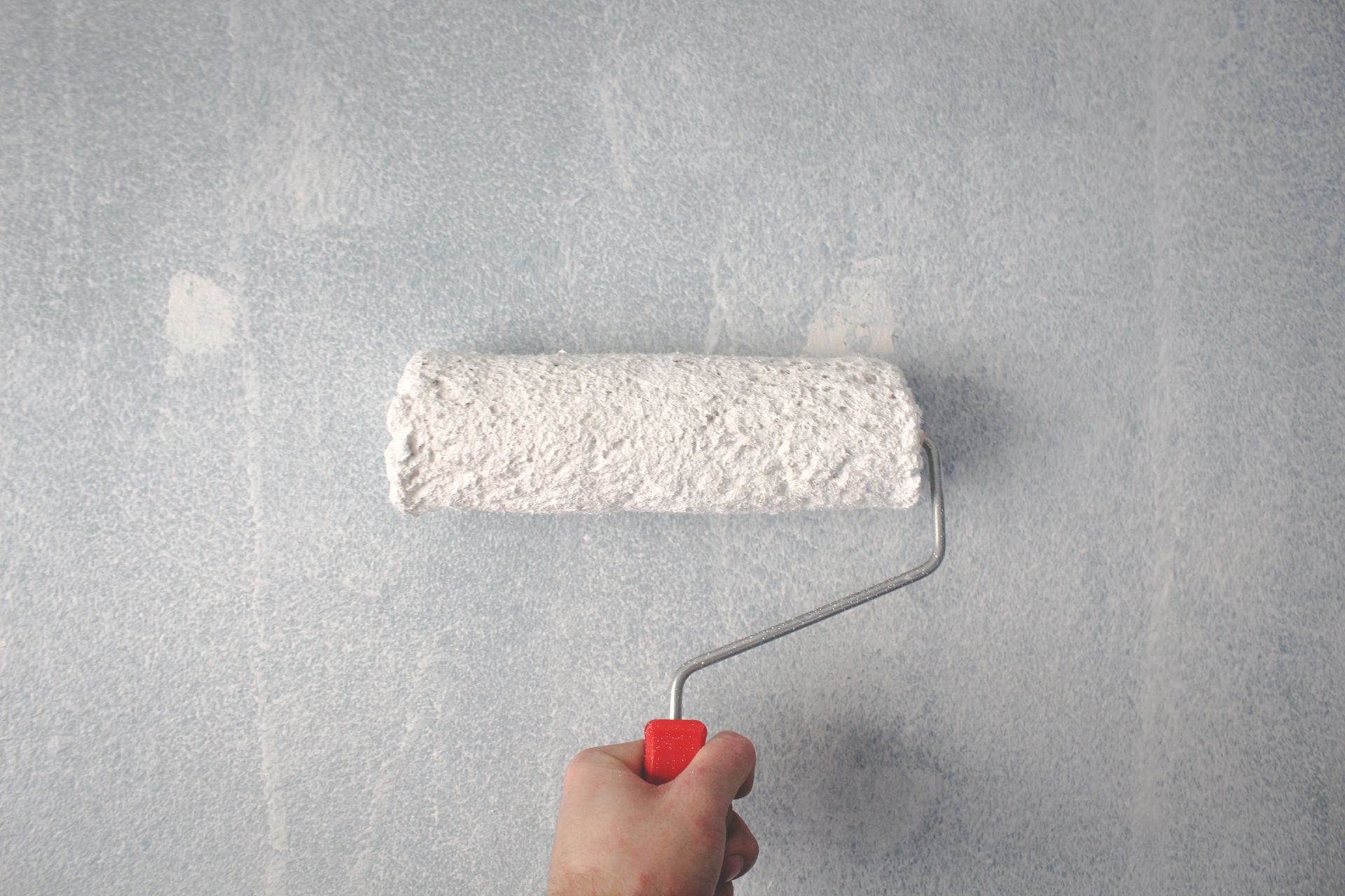 Paint roller applying white paint to an interior wall